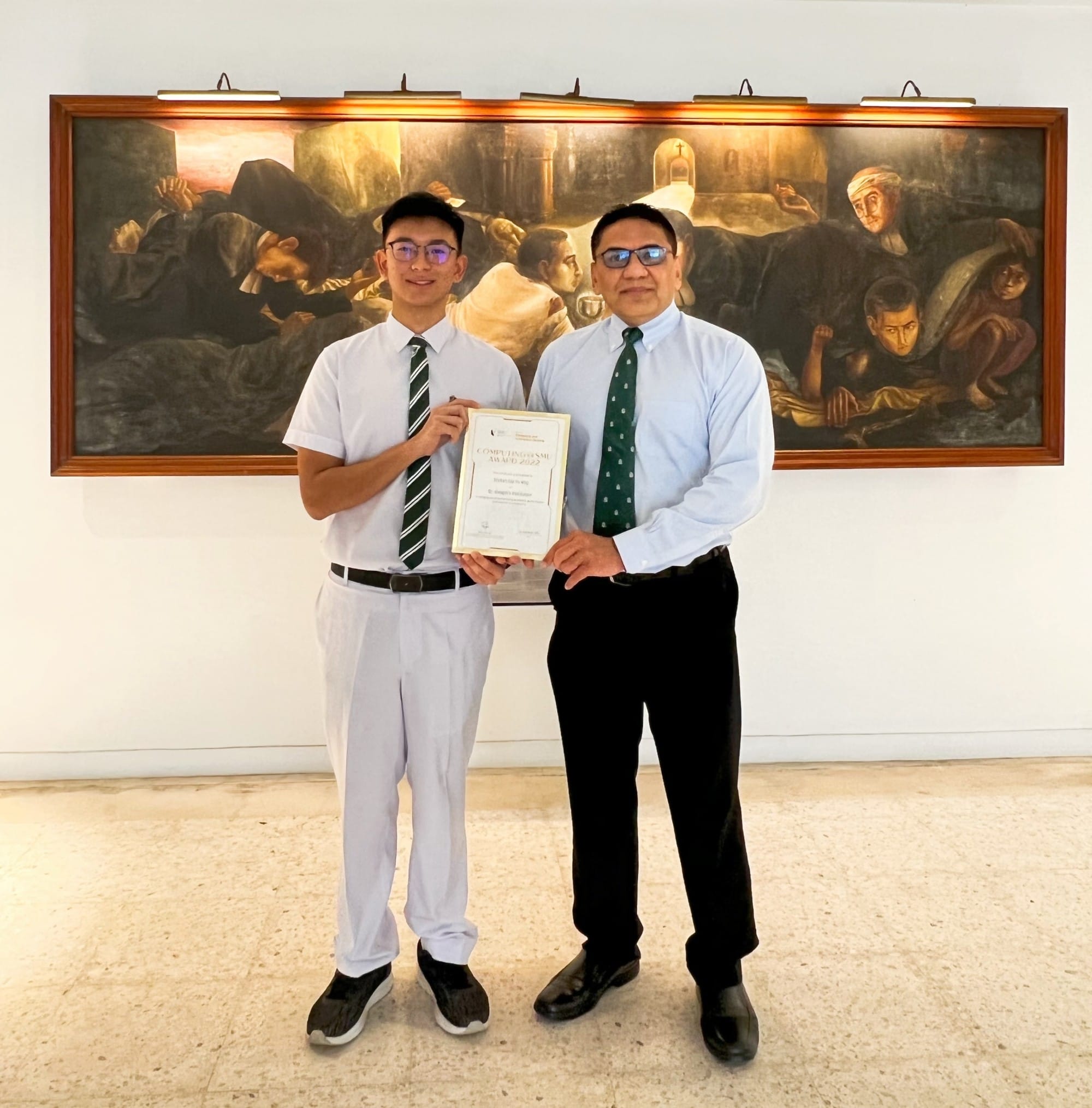 Two men in shirts and ties hold a certificate together, standing before a large dark painted mural on a white wall.